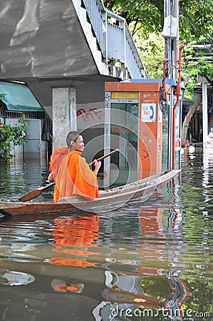 A young buddhist monk keeps smiling as he is rowing his boat in a flooded street of Bangkok, Thailand on the 11th of November 2011 Editorial Stock Photo