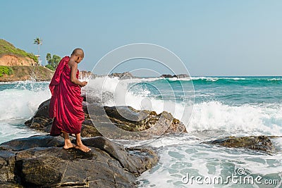 A young Buddhist monk stands on a rock in the ocean. Sri Lanka Editorial Stock Photo