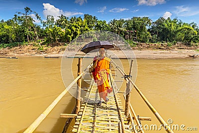 A young Buddhist monk walks across a bamboo bridge over Nam Khan in Luang Prabang Laos Editorial Stock Photo