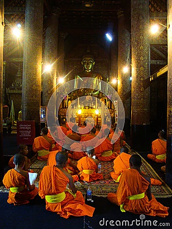 Young Buddhist monks pray at large gold Buddha statue, Laos Editorial Stock Photo