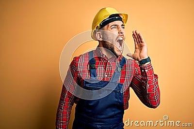 Young builder man wearing construction uniform and safety helmet over yellow isolated background shouting and screaming loud to Stock Photo