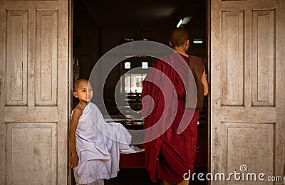 Young Burmese monk in white robe at Maha Gandaryon monastery waits at dining hall door Editorial Stock Photo