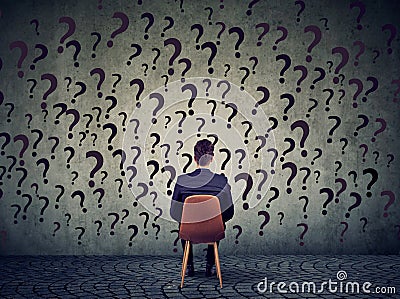 Business man sitting on a chair in front of a wall has many questions, wondering what to do next Stock Photo