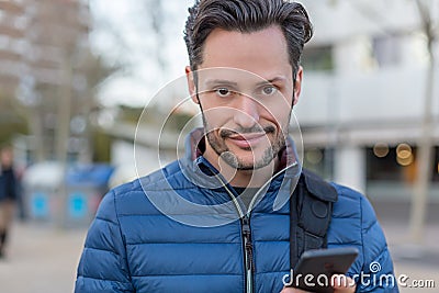 Young business smiling man in the street with a cellphone and a blue jacket Stock Photo