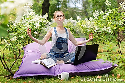 Young business woman doing yoga outside office building sitting in lotus position in the park with her laptop and cup of tea or co Stock Photo