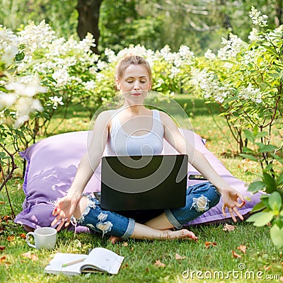 Young business woman doing yoga outside office building sitting in lotus position in the park with her laptop and cup of tea or co Stock Photo