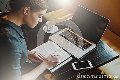 Young business woman in gray dress sitting at table in cafe and writing in notebook. Stock Photo