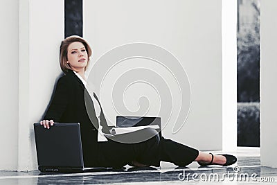 Young business woman with laptop sitting at the wall Stock Photo