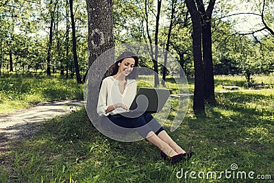 Young business woman sitting on a ground and working on her laptop in a public park and smiling Stock Photo