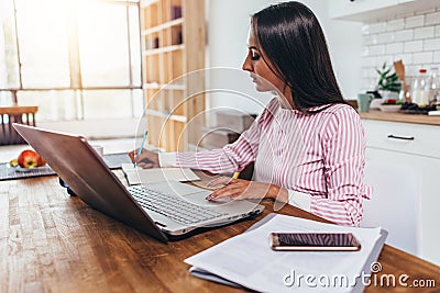 Young business woman sitting at table in kitchen and writing in notebook. Student learning online. Stock Photo