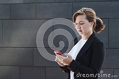 Young business woman in a business suit looks upset and displeased at the phone. girl receives and reads bad news. lady looks Stock Photo