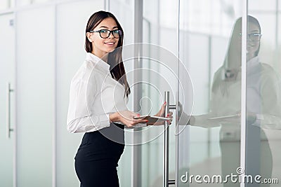 Young business woman with tablet computer opening glass office door Stock Photo