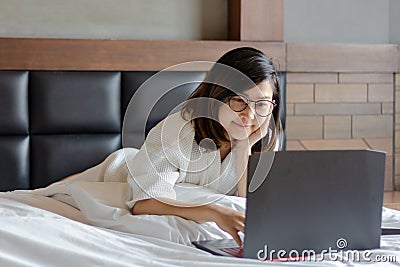 Young business woman talking on phone and using moble phone on bed while working from home during covid -19 crisis Stock Photo