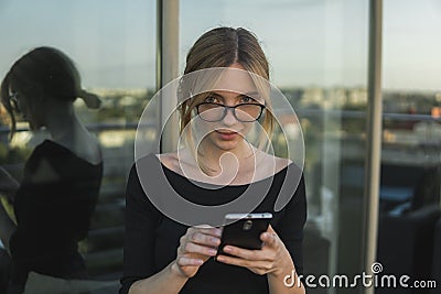 Young business woman uses phone. Good looking brunette female uses online banking on smart phone to transfer money from Stock Photo