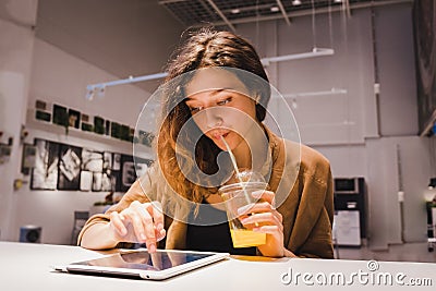 Young business woman uses a tablet and drinks freshly squeezed orange juice from a straw in a cafe Stock Photo