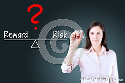 Young business woman writing question with risk compare to reward on balance bar. Blue background. Stock Photo