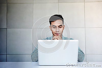 Young Businessman in Casual Shirt Working on Computer Laptop in Office. Hand on Shin, Sitting on Desk. Concentrated in Computer Stock Photo