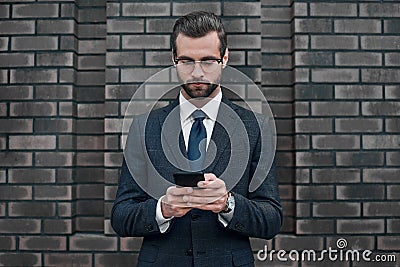 A young businessman in glasses and an expensive suit, works on a smarphone in his hands Stock Photo