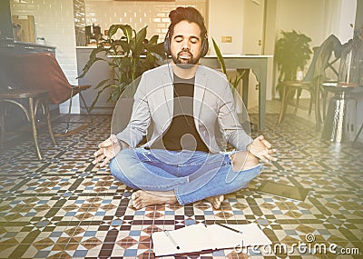 Young businessman in headphones meditating in lotus pose taking a deep breath at living room.Business yoga and stress Stock Photo