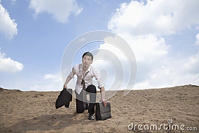 Young businessman kneeling in the desert and holding a briefcase, exhausted Stock Photo