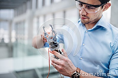 A young businessman or scientist with robotic hand standing in office, working. Stock Photo