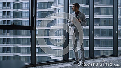 Young businessman searching tablet computer standing by window in office centre. Stock Photo