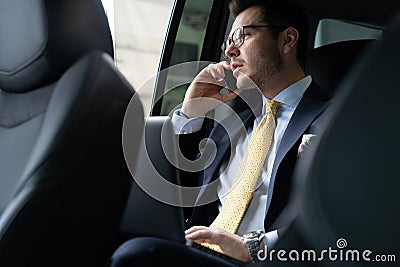 Young businessman sitting on back seat of the car, while his chauffeur is driving automobile. Stock Photo