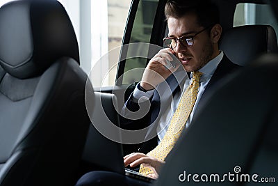 Young businessman sitting on back seat of the car, while his chauffeur is driving automobile. Stock Photo