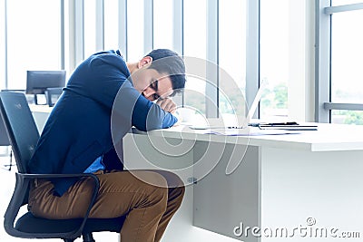 A young businessman sitting in a modern office. He has a feel sleepy because hard work so tired weary fatigued and exhausted. On Stock Photo