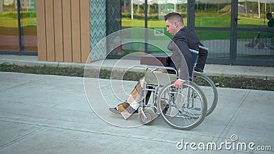 Young businessman in a suit in a wheelchair. A serious man is riding in a wheelchair against a business center. Special Stock Photo