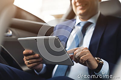 Young businessman using tablet pc while sitting on back seat of a car. Caucasian male business executive by a taxi and Stock Photo