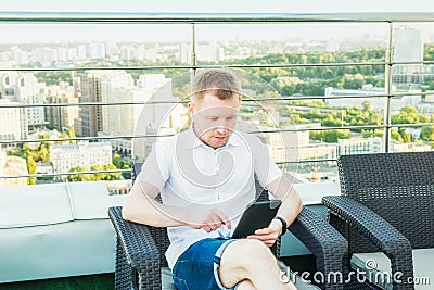 Young businessman working on laptop tablet comfortably sitting on chair on the office terrace balcony with Urban Landscape on Back Stock Photo