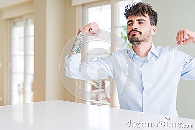 Young businesss man sitting on white table showing arms muscles smiling proud Stock Photo