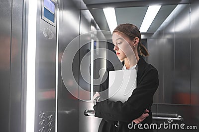 Young businesswoman is concentrated on lookinig at the floor number in the elevator holding her laptop. Female office worker in Stock Photo