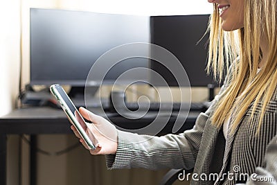 Young businesswoman holding a cellphone and reading emails from home with a business desktop on th background. Successful woman Stock Photo