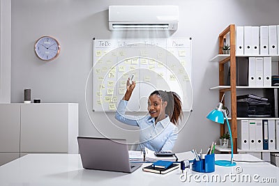Businesswoman Operating Air Conditioner In Office Stock Photo