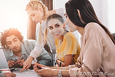 young businesswoman pointing by finger on graphs to male colleague while two businesswomen talking to each other at modern Stock Photo