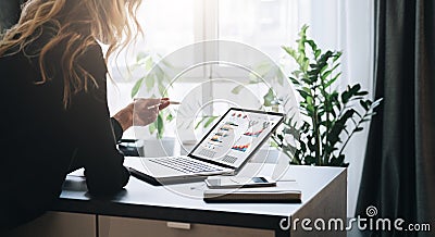 Young businesswoman is standing near table, pointing pencil on graphs, charts, diagrams, schedules on screen of computer Stock Photo