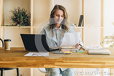 Young businesswoman woman is sitting at kitchen table, reading documents,uses laptop,working, studying. Stock Photo