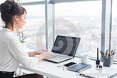 Young businesswoman working in office, typing, using computer. Concentrated woman searching information online, rear Stock Photo