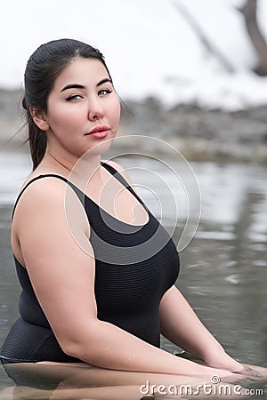Young busty curvy full figured young model in black swimsuit sitting in outdoors pool at spa resort Stock Photo