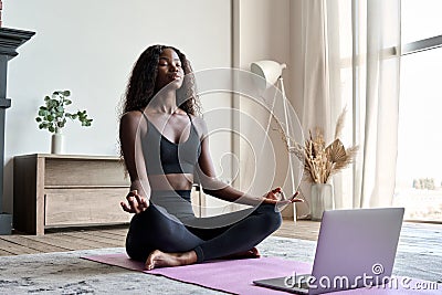 Young calm fit healthy African black woman at home doing yoga learning online class. Stock Photo