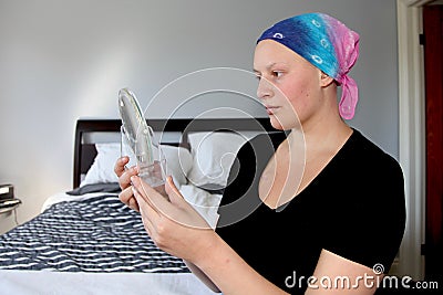 Portrait of a young cancer patient in a headscarf looking at self in mirror Stock Photo