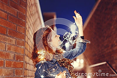 Young carefree redhead woman playing with fairy lights outdoors Stock Photo