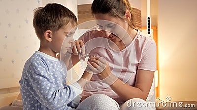 Young caring mother cutting off fingernails to her son before going to bed at night Stock Photo