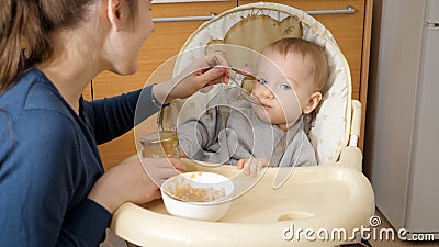 Young caring mother giving porridge to her baby son with spoon Stock Photo