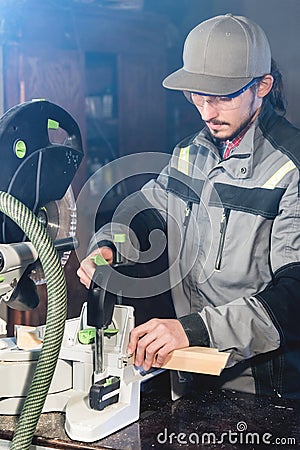 A young carpenter installs a wooden workpiece in a circular sawing machine. Home workshop. Novice businessman Stock Photo