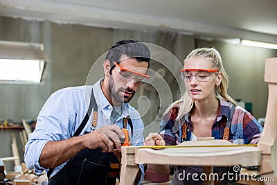 young carpenter man and women using measuring tape looking wood size at workspace. craftsman profession in wood factory Stock Photo