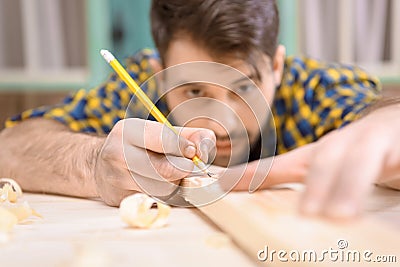 Young carpenter with pencil measuring and marking wooden plank Stock Photo