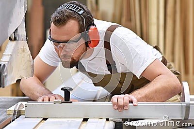 Young carpenter in working clothes works in the joinery on a san Stock Photo